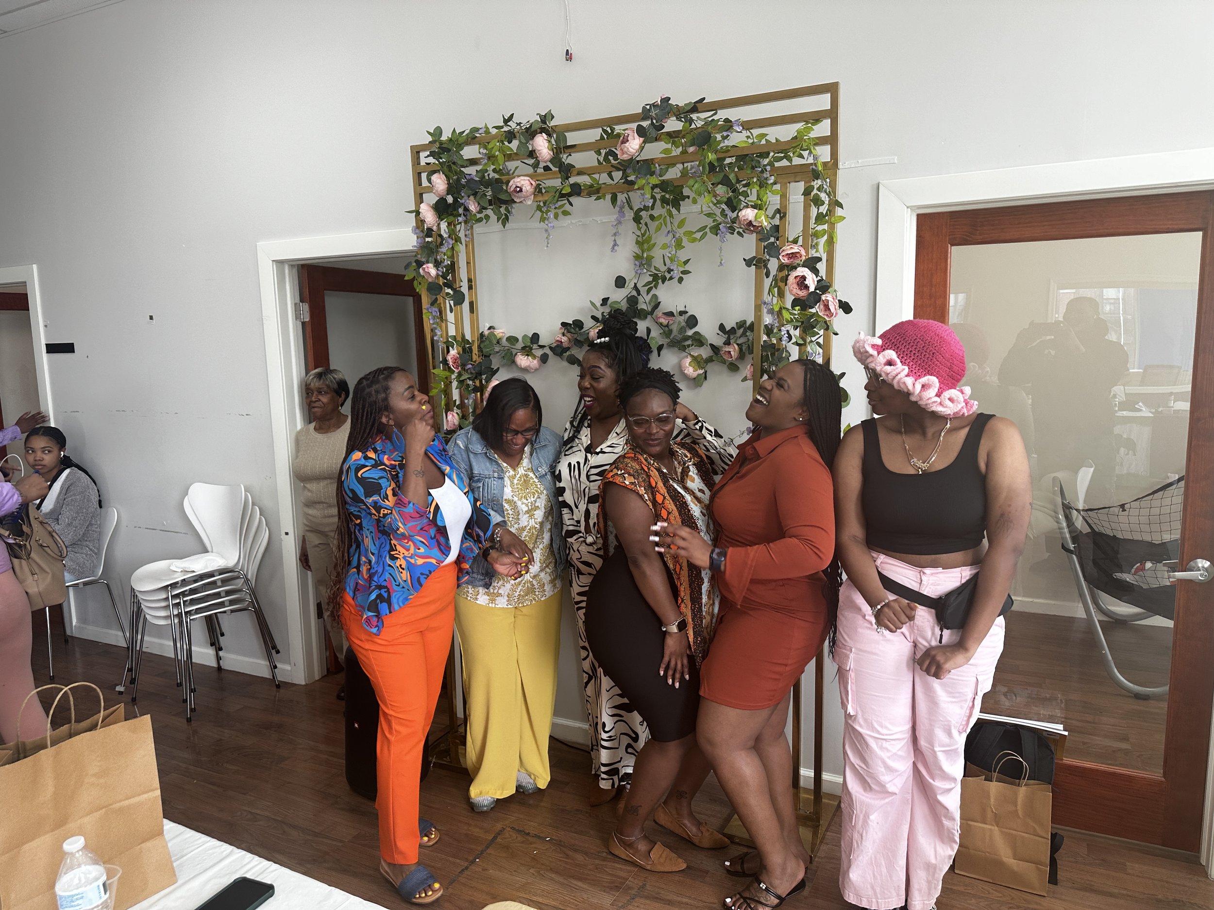 Group of seven women standing in front of a floral decoration at a social gathering.