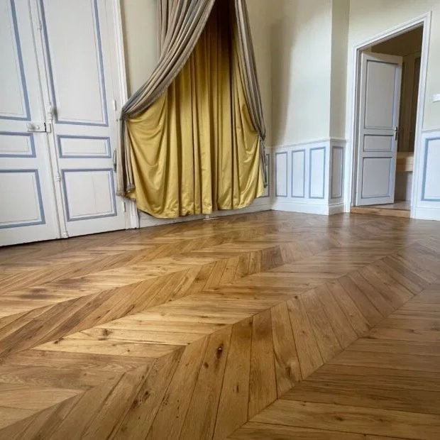 Intérieur d'une pièce avec un parquet en chevrons, des rideaux dorés, des portes blanches et un mur avec des moulures blanches et bleues.