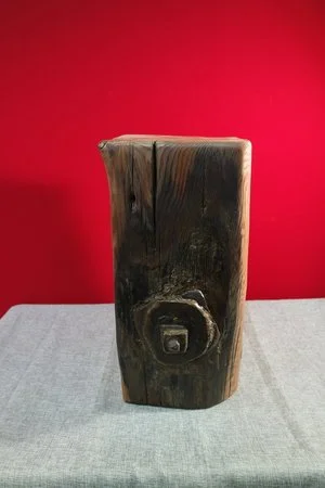 Une pièce en bois brut avec une finition foncée, posée sur une surface en tissu gris clair, contre un mur rouge vif.
