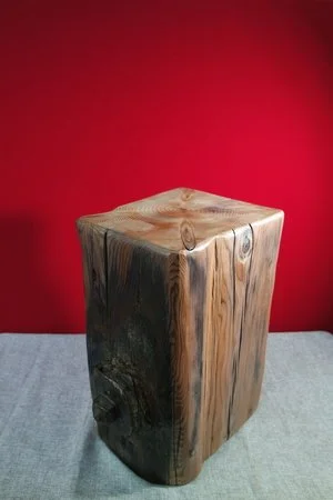 Un cube en bois massif avec des veines naturelles, posé sur une surface plate, contre un mur rouge.