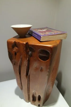 Un socle en bois avec une coupe blanche et un livre posé dessus.