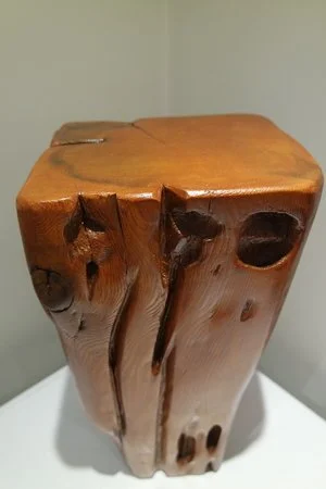 Statue en bois avec une finition lisse et quelques détails naturels, placé sur une surface blanche.