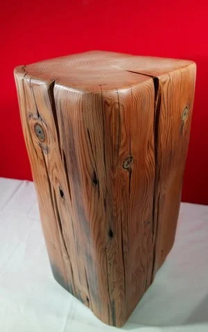 Cube en bois clair avec des veines visibles, placé sur un sol blanc, avec un fond rouge.