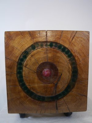 Une boîte en bois carré avec un motif circulaire en son centre, posée sur une surface blanche.