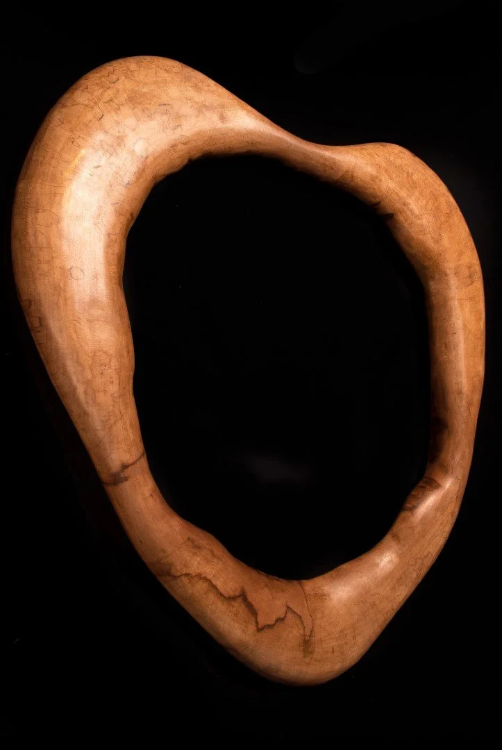 Un objet en bois sculpté en forme de cœur ou de boucle tranchée, posé sur un fond noir.