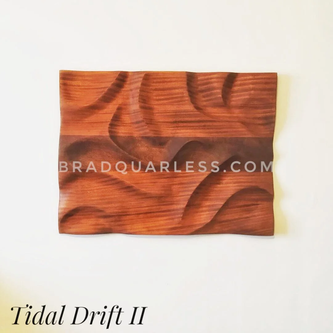 Une œuvre en bois intitulée 'Tidal Drift II' avec des motifs de vagues sculptés dans le bois, posée contre un mur blanc.