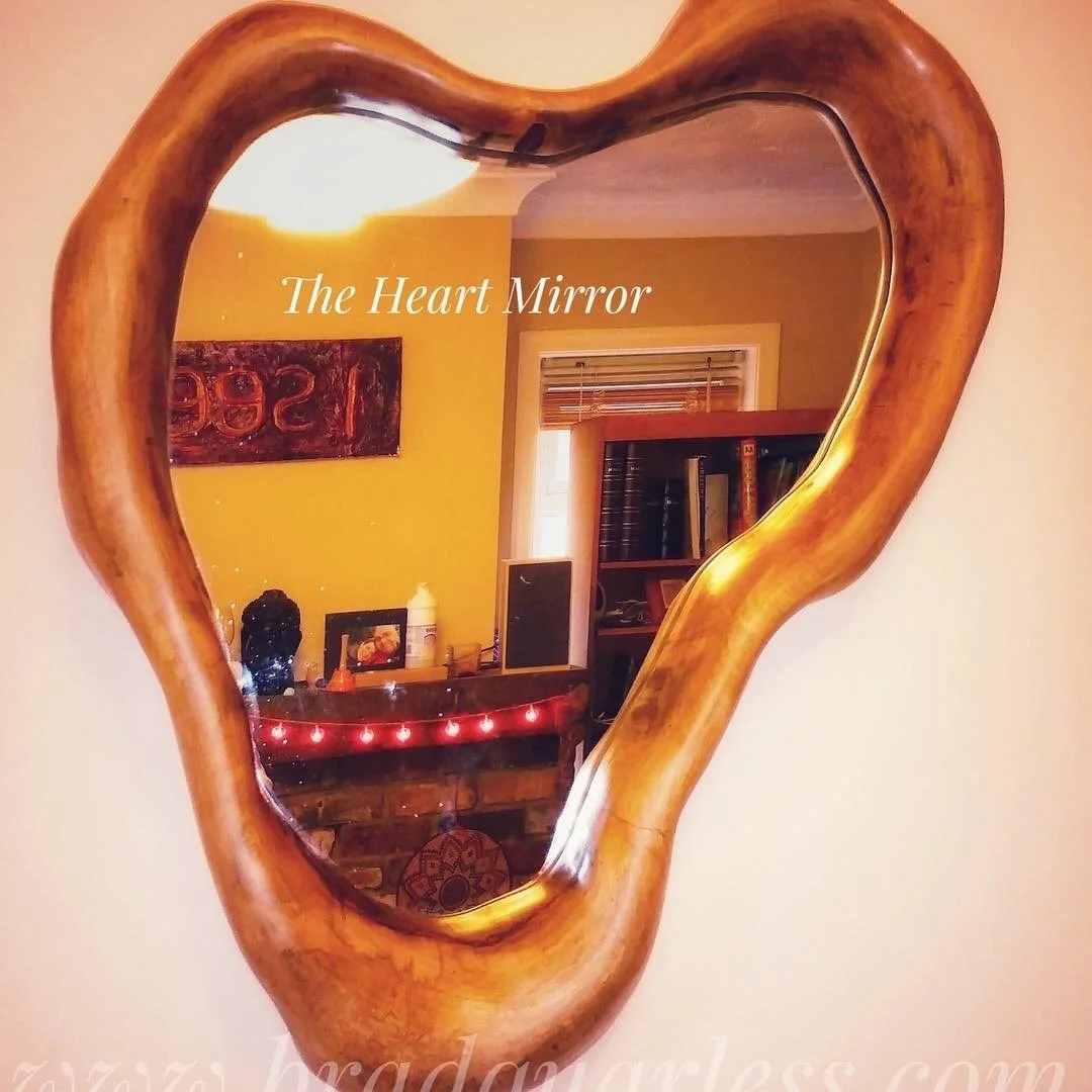 Miroir en forme de cœur dans un cadre en bois, reflétant une pièce avec des meubles, des livres et des décorations.