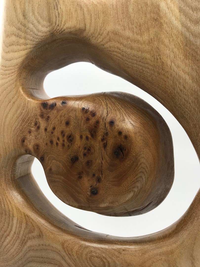 Vue rapprochée d'une sculpture en bois avec des formes courbes et des nœuds dans le bois.