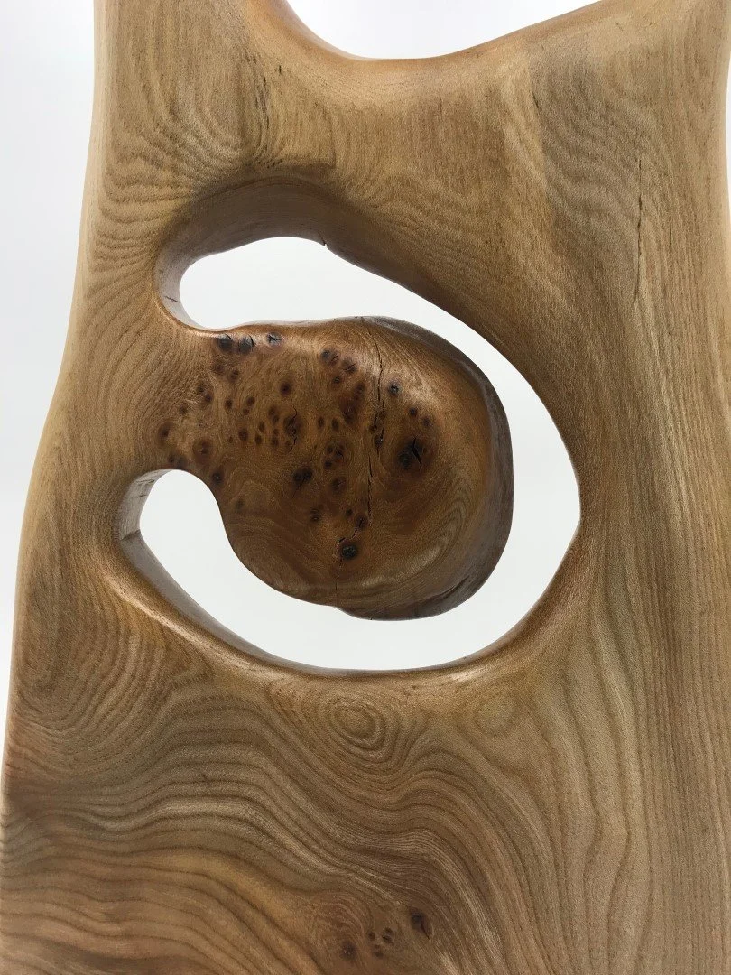 Détail d'une sculpture en bois avec des formes courbes et des trous, mettant en valeur la texture et le grain du bois.