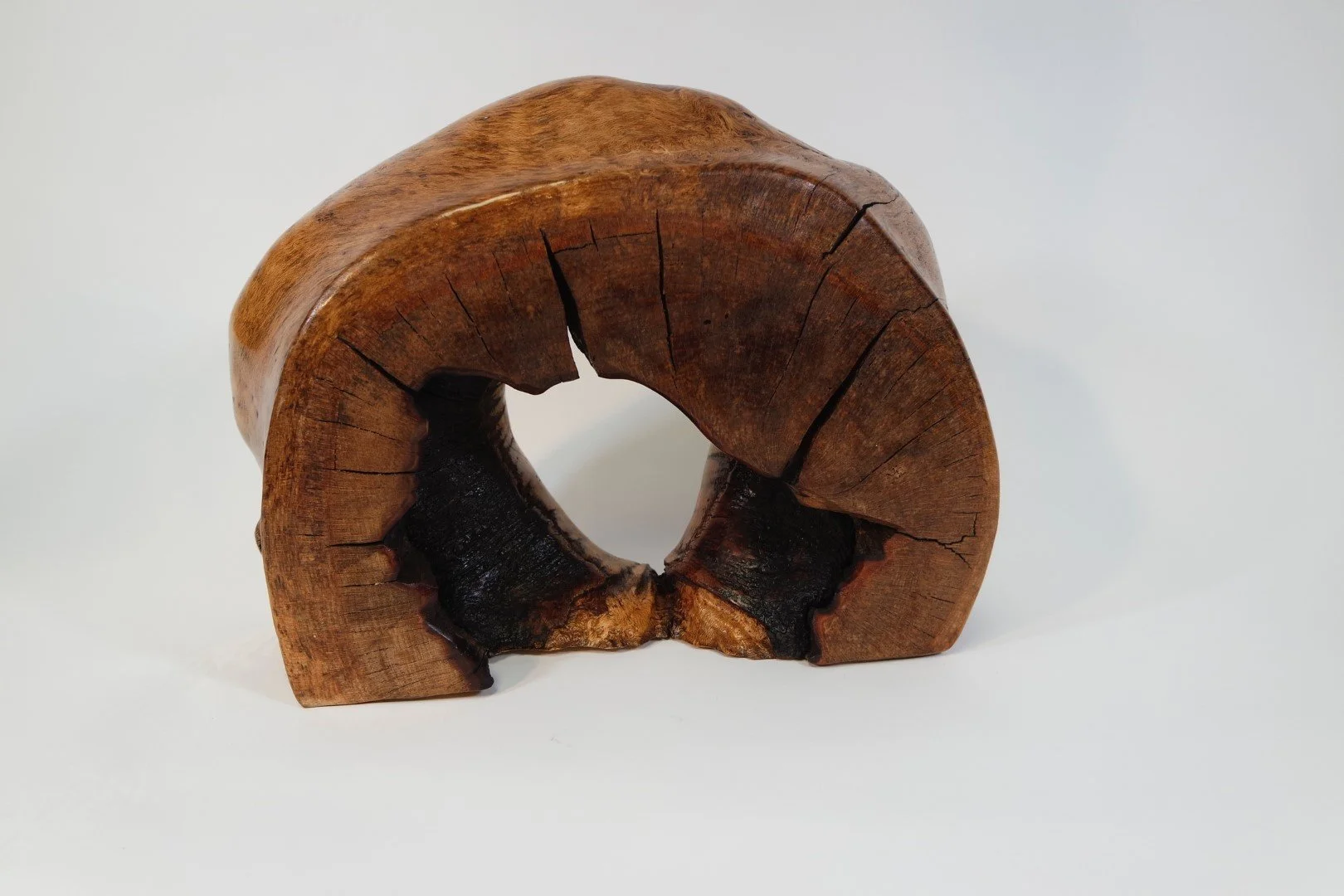 Une sculpture en bois en forme de rouleau, avec des fissures et des parties brûlées, placée sur un fond blanc.