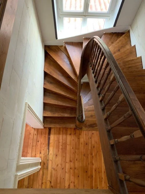Escalier en bois tournant vu du haut avec une fenêtre à proximité