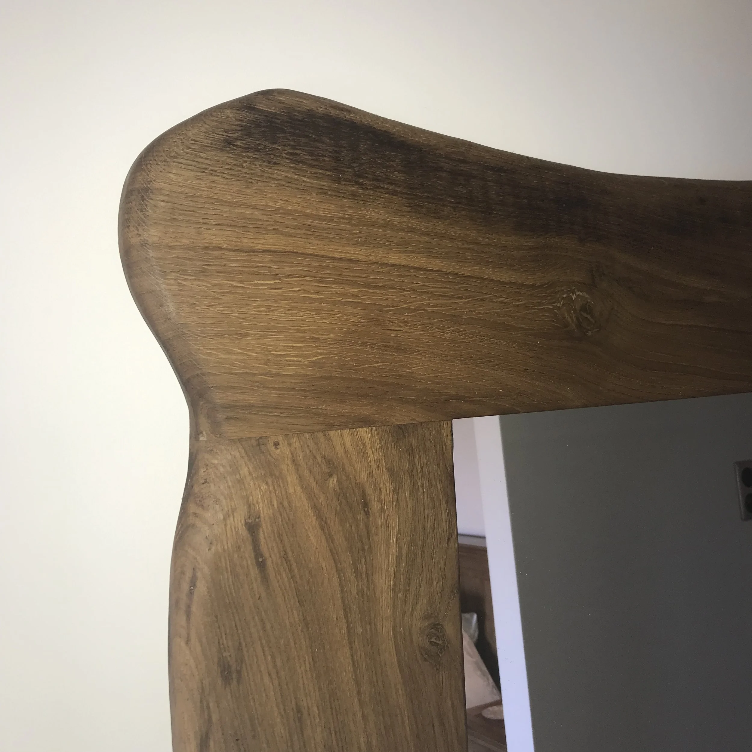 Une photo d'un meuble en bois avec une surface lisse et visible les veines du bois, vue de côté avec un mur blanc en arrière-plan.
