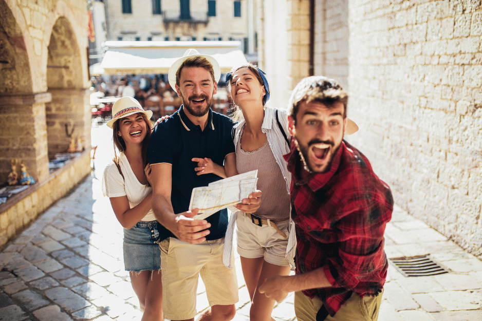 Quattro amici sorridenti che esplorano una città storica, uno con una mappa, in una via soleggiata.