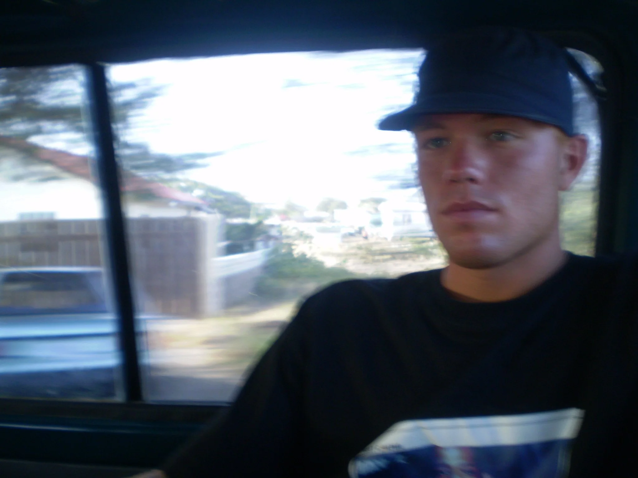 Roland Carter wearing a dark baseball cap and black shirt, sitting in a vehicle with trees and houses visible outside through the window.