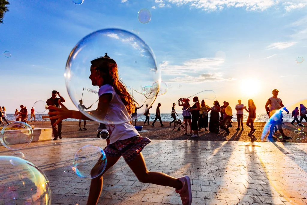 A girl running on a beach promenade surrounded by bubbles at sunset.