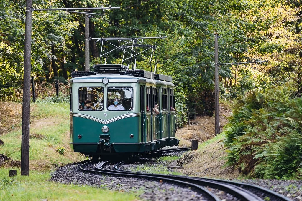 A small green train on a track and rail track going around the hills of Switzerland.