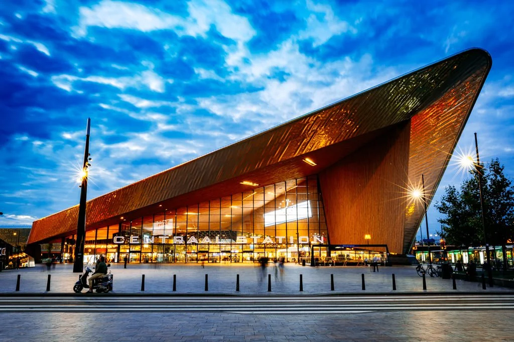 Modern train station with a distinctive wooden facade, glass entrance, and lit street lamps at dusk.