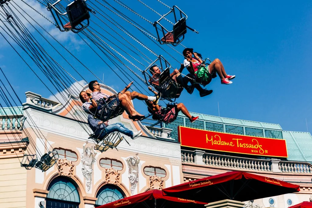 People riding a swing carousel in front of a Madame Tussauds wax museum.