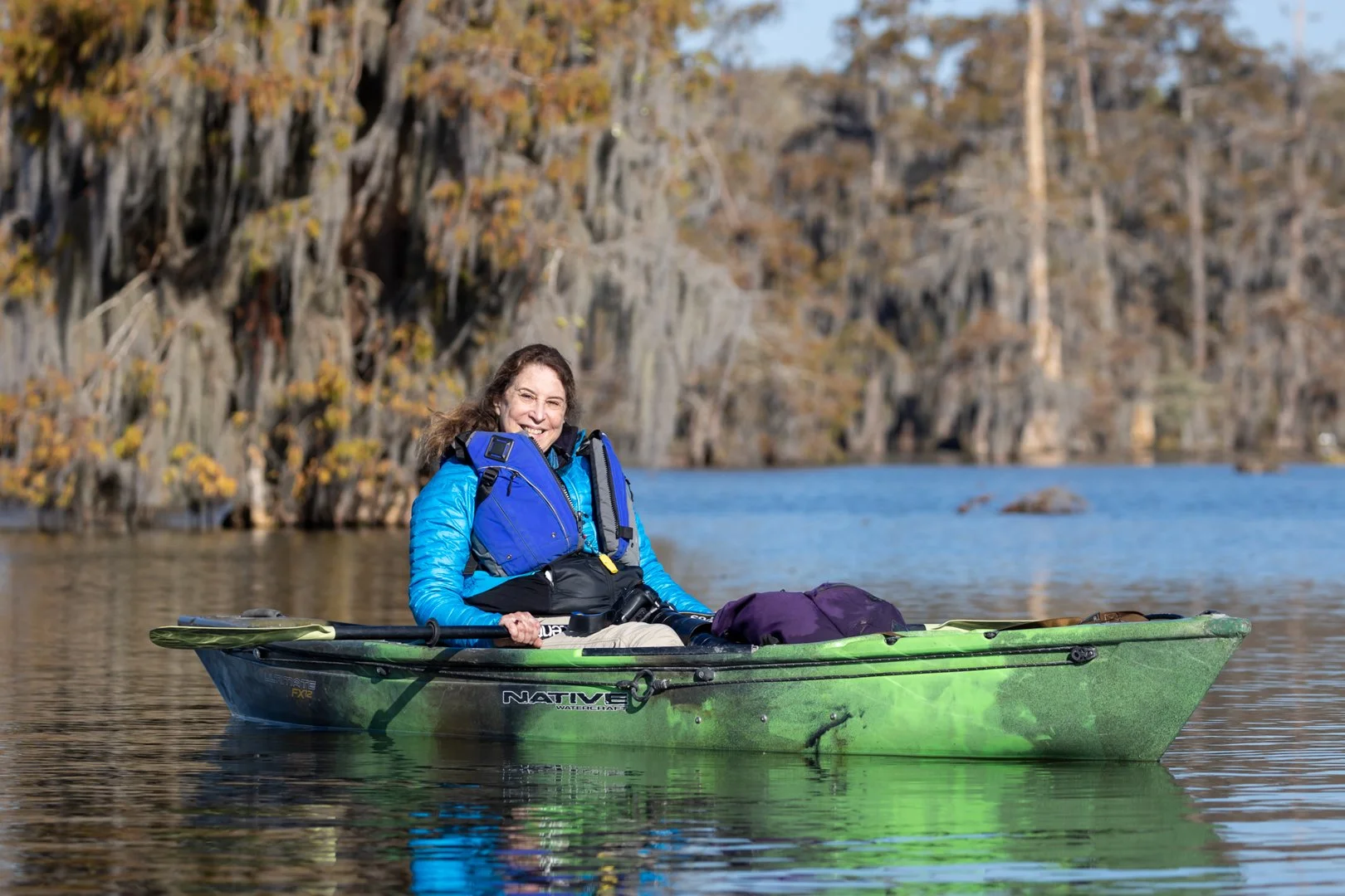 Woman photographer in green kayak with cypress swamp behind her