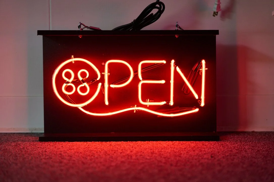 Loving Stitches in Fayetteville commissioned this playful OPEN sign from us, incorporating a button and thread into the design.  Made of clear tubing with red neon gas, this is sure to catch attention from folks driving past on US-401.