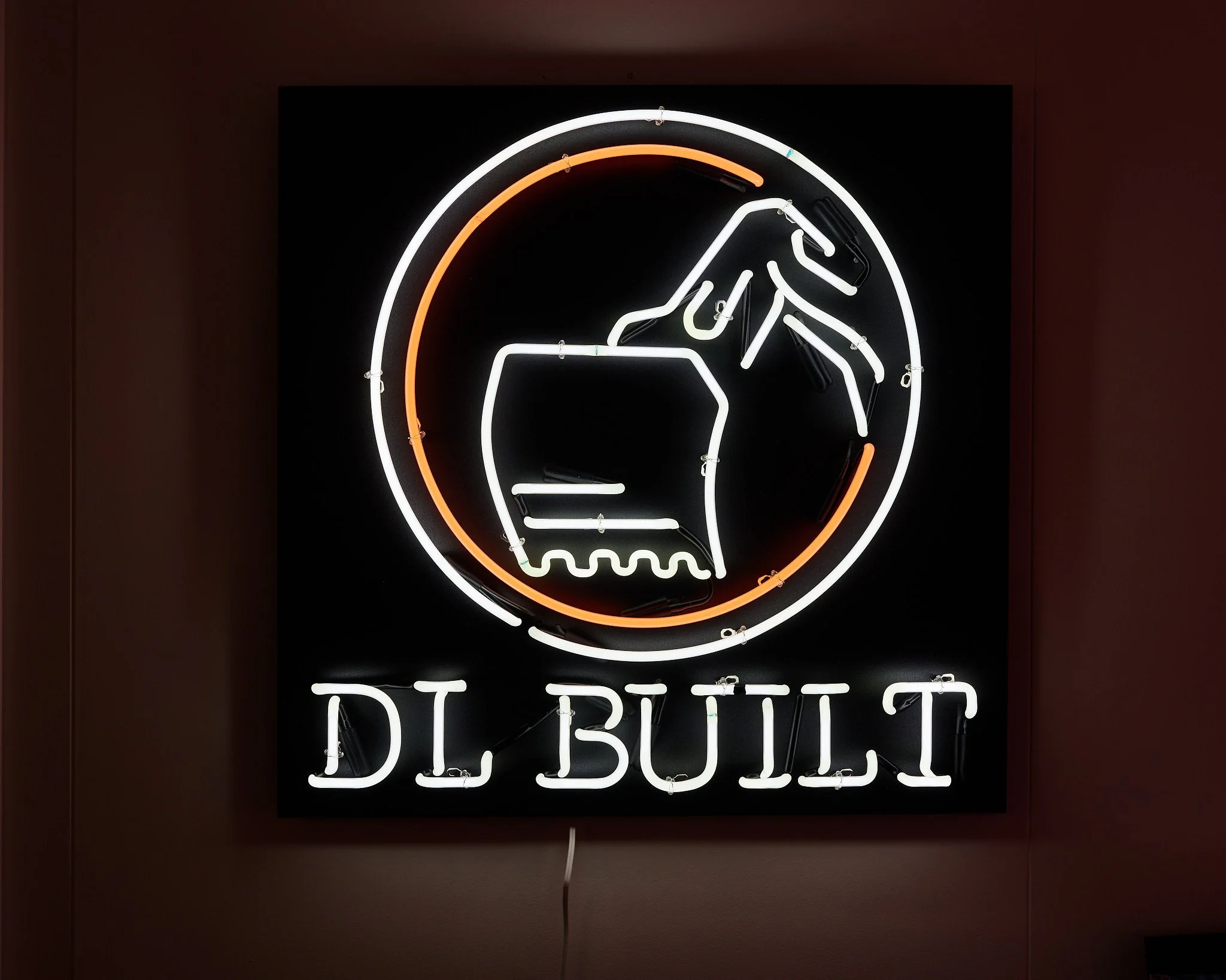 A repeat customer came to us with a request to create their business logo in neon; we matched the typeface of their logo and their construction scoop in cool white neon, and added an orange accent circle using yellow-green tubing pumped with red neon