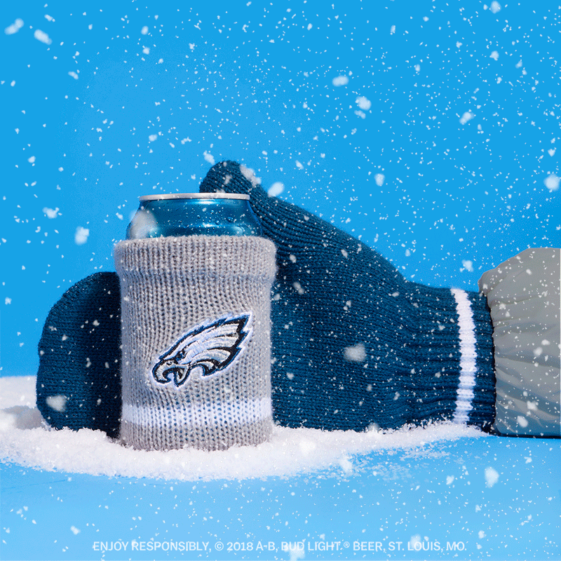 A can of Bud Light beer wrapped in an Eagles-themed sock, held by a person wearing a blue and white glove, against a snowy blue background.