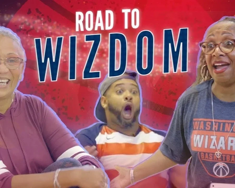 Three people smiling at a Washington Wizards game and in an excited mood with a vibrant red background that has the text 'Road to Wizdom' in bold letters. AARP
