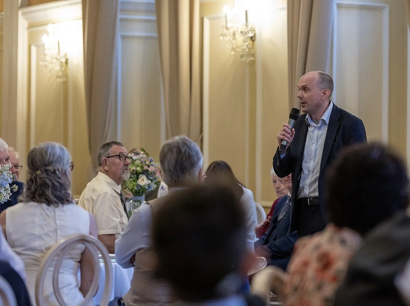 David Richards MCs a wedding at the Assembly House in Norwich, speaking into a  microphone to the audience at the wedding breakfast..
