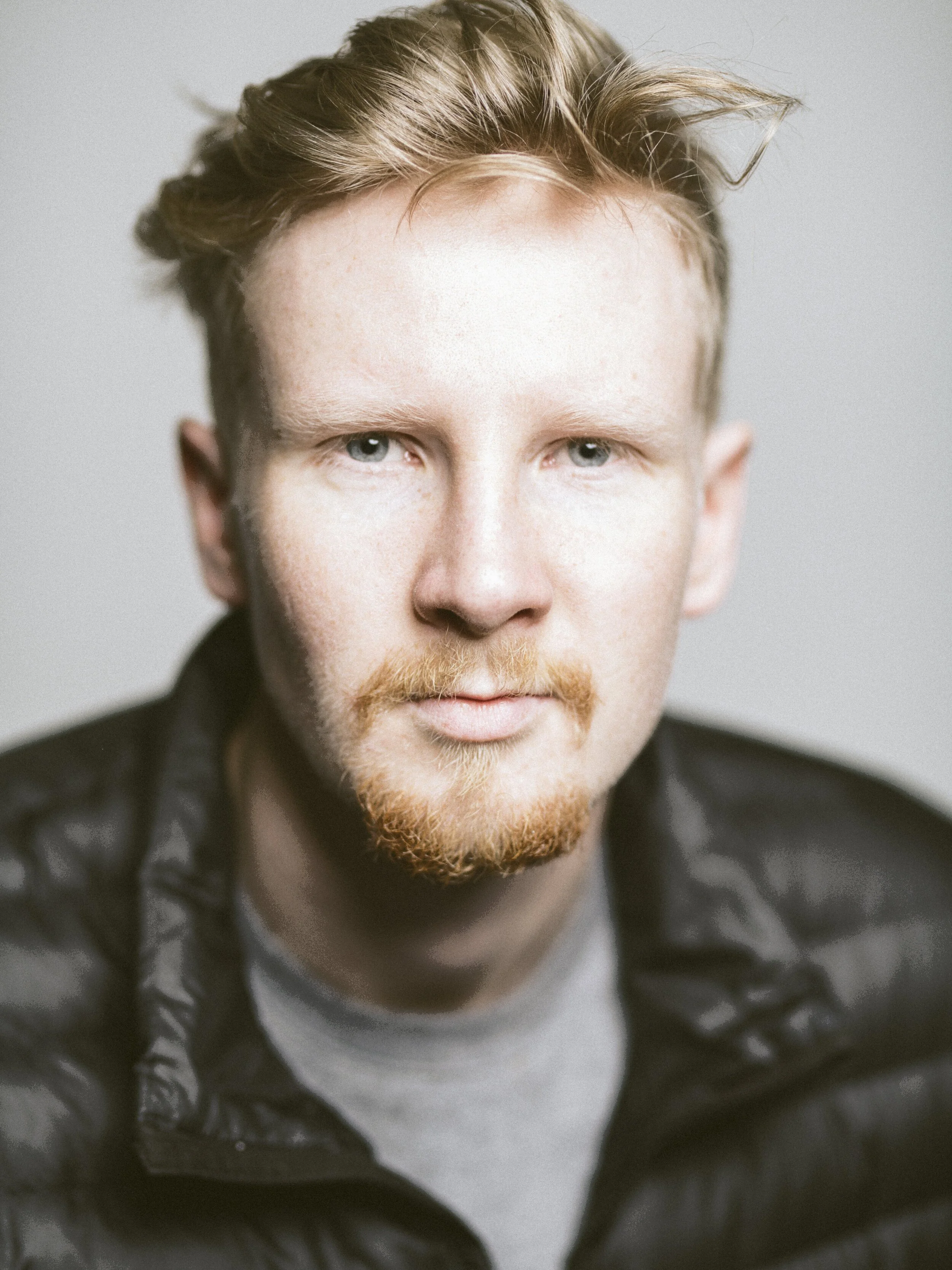 Portrait of a man with light-colored hair and beard wearing a black jacket
