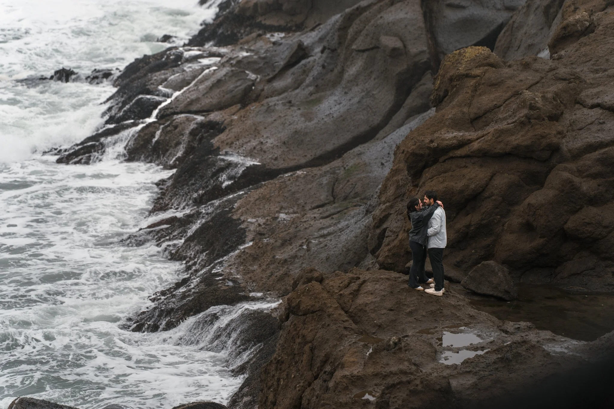 A couple standing on the rocks near the ocean waiting on a picture by their proposal photographer