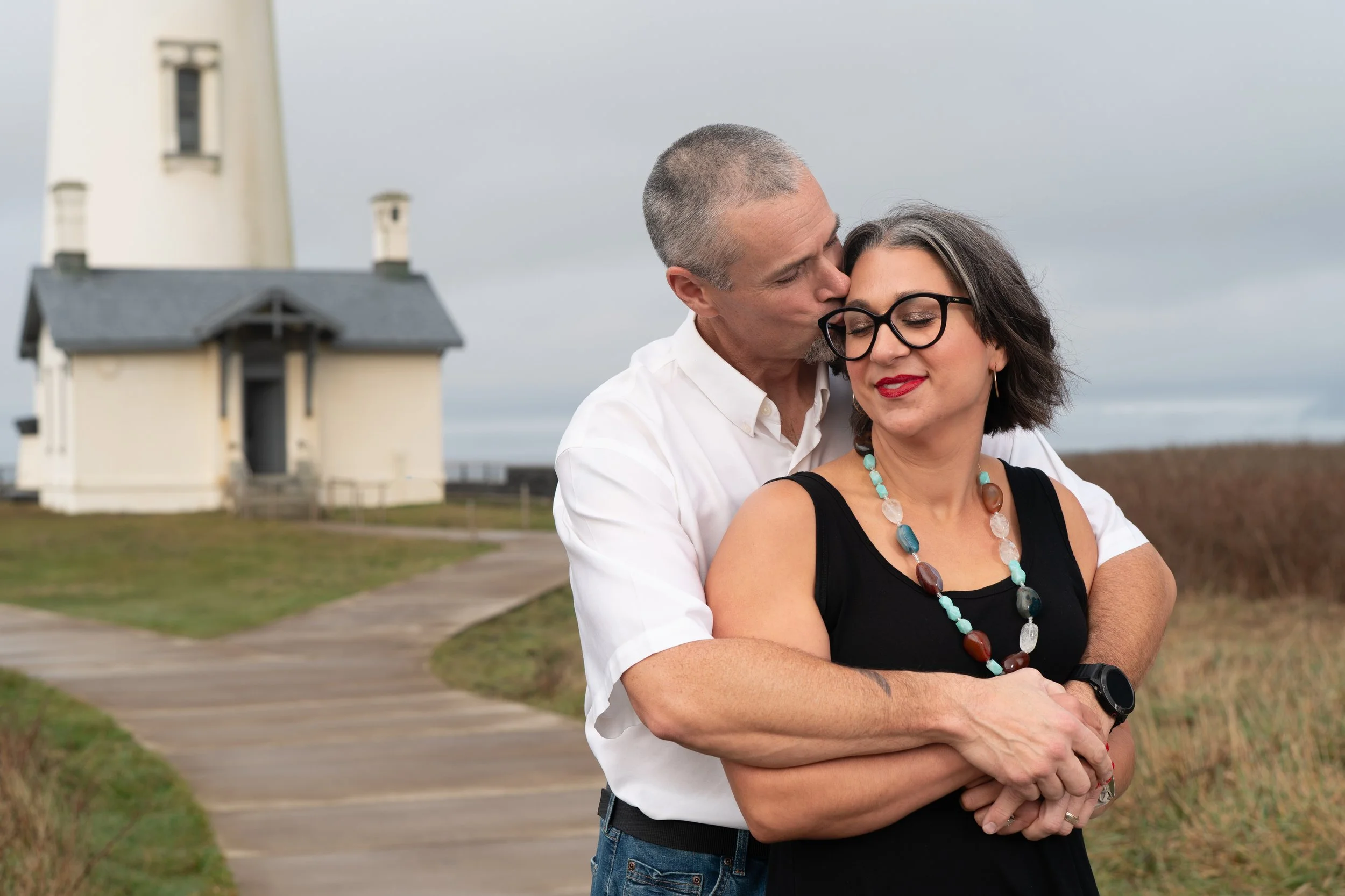 husband and wife hugging by the lighthouse in newport oregon