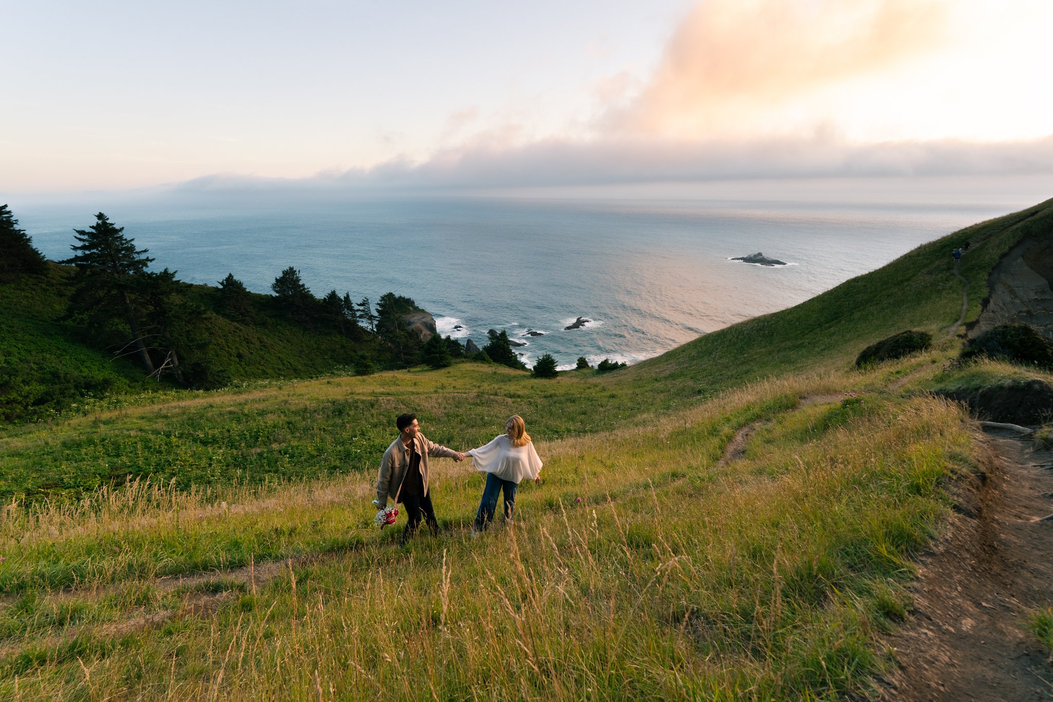 a couple walking through the meadow on the way from the knoll to god's thumb after a proposal in lincoln city oregon