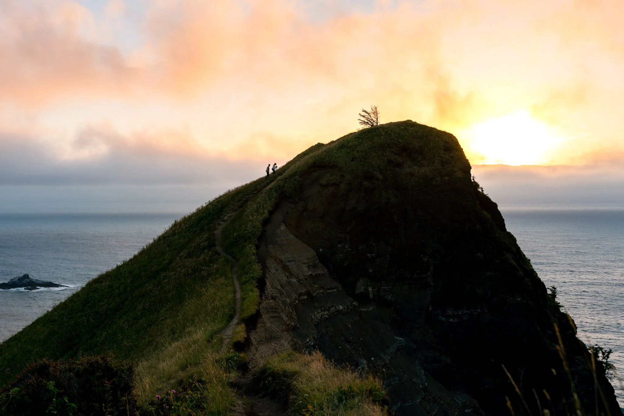 a couple hiking up to the top of god's thumb during the sunset in lincoln city oregon