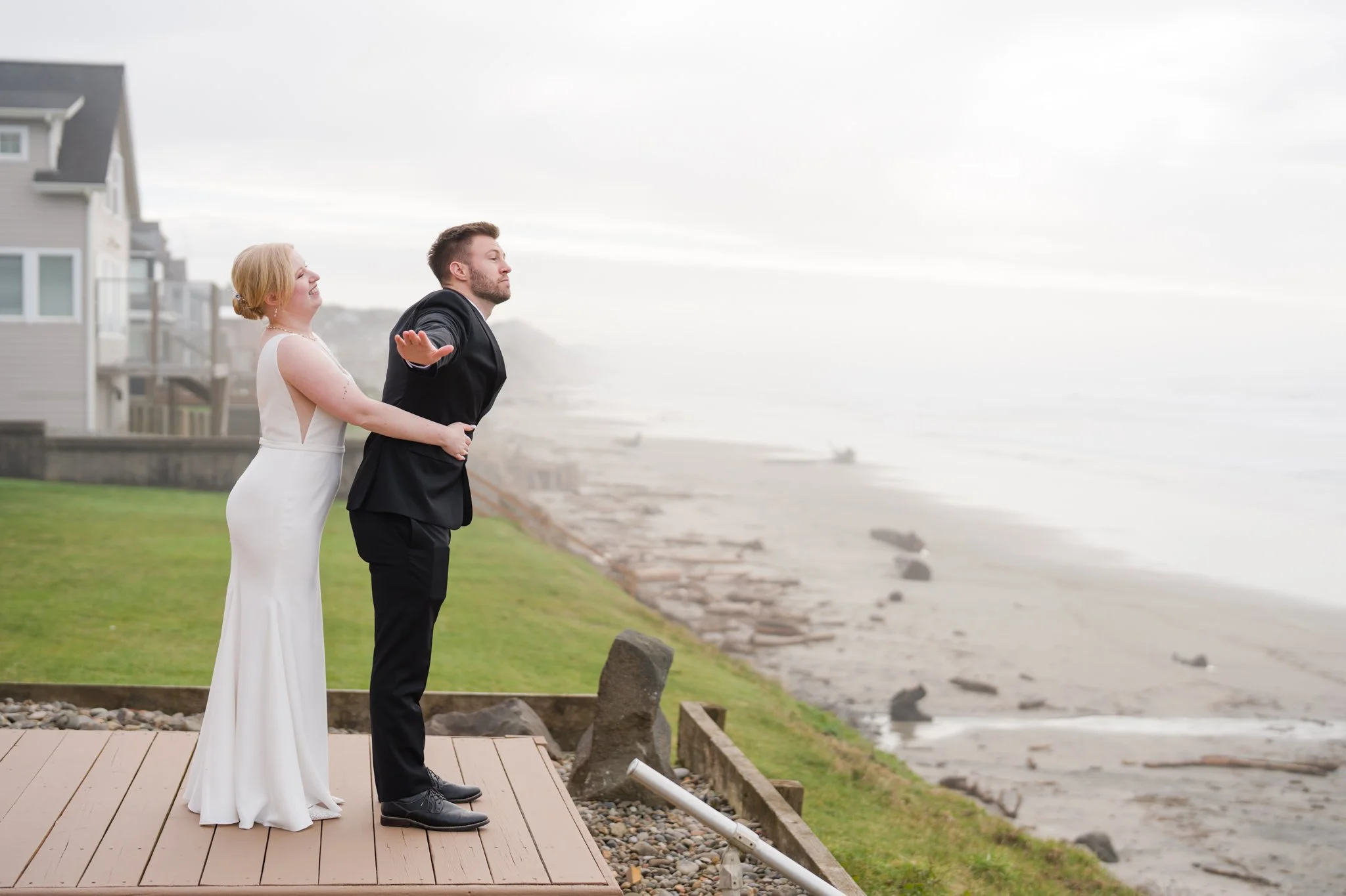 Playful bride and groom sharing a candid moment on a beach-view Airbnb patio in Lincoln City, Oregon, with Roads End Beach and God’s Thumb in the background.
