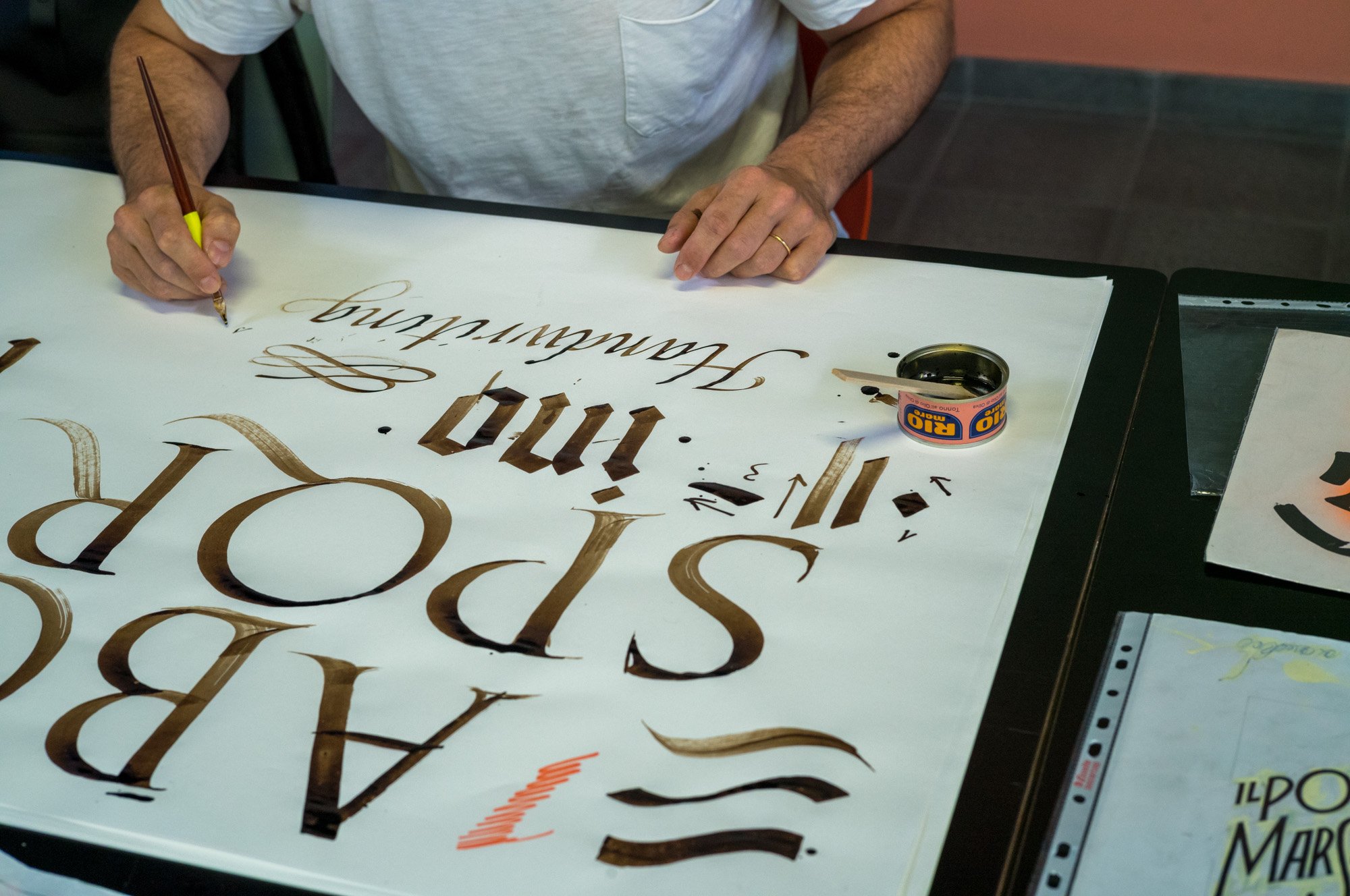 Andrea Carrer creating calligraphy art on a large white sheet of paper with a brush and brown ink in the studio at Tipoteca Italiana.