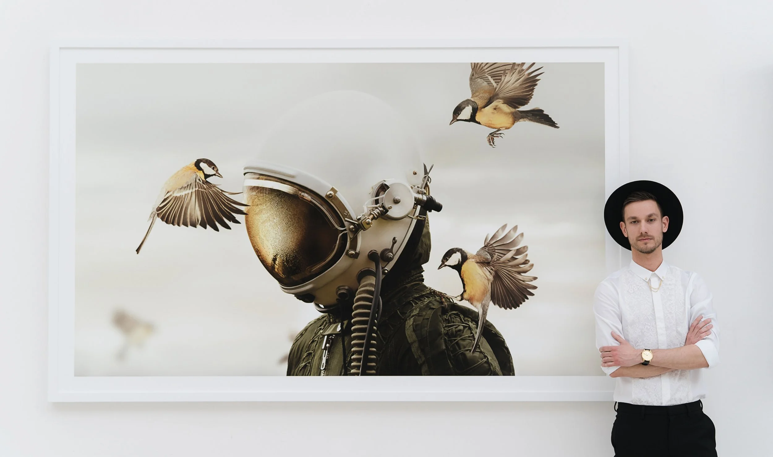 Man standing next to framed artwork of an astronaut helmet with birds flying around it.