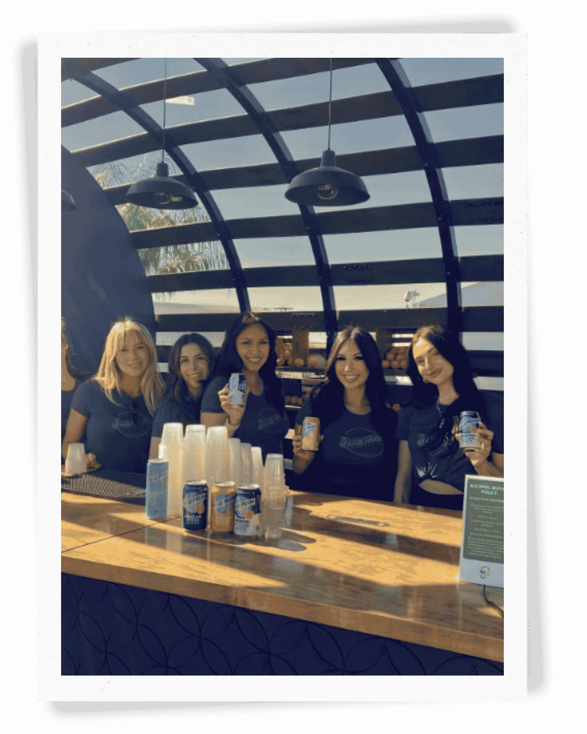 A team of EPI Promotions Brand Ambassadors in Blue Moon branded uniforms smiling behind a sampling bar at an outdoor festival activation, showcasing large-scale beverage event staffing by a national brand ambassador agency.