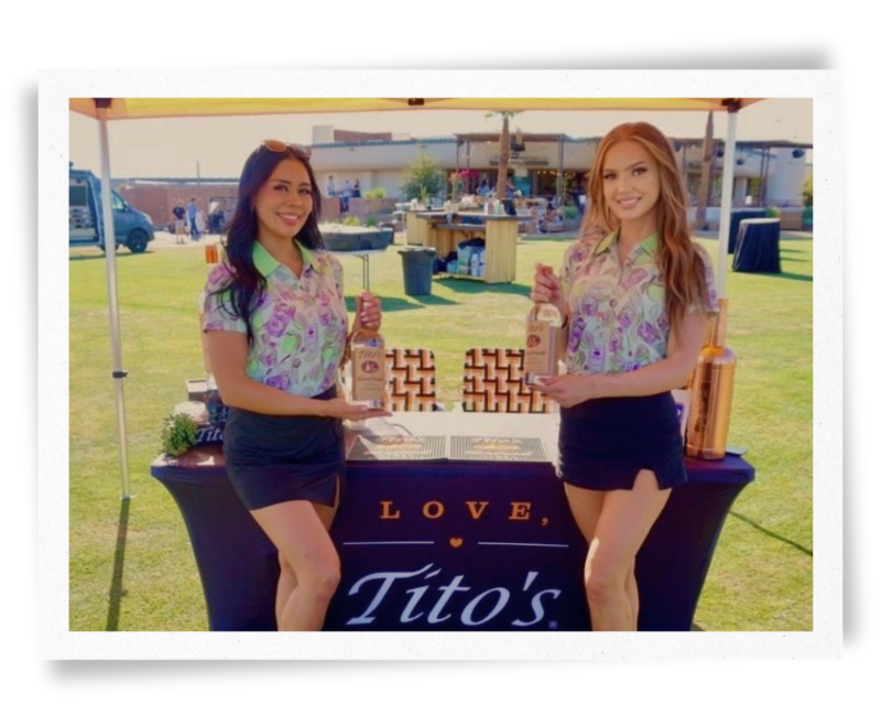 Two EPI Promotions Brand Ambassadors in branded floral uniforms representing Tito's Handmade Vodka at an outdoor premium sampling activation, showcasing the polished, professional standard expected of every Brand Ambassador on our team.