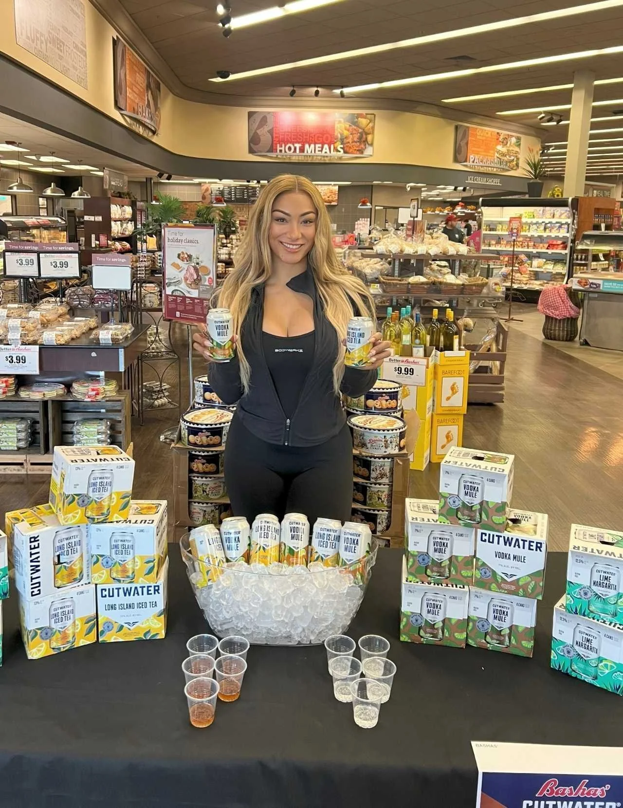 EPI Promotions brand ambassador at a Cutwater Spirits off-premise sampling activation inside a grocery store, holding Cutwater canned cocktails surrounded by branded product displays for a national brand ambassador staffing agency.