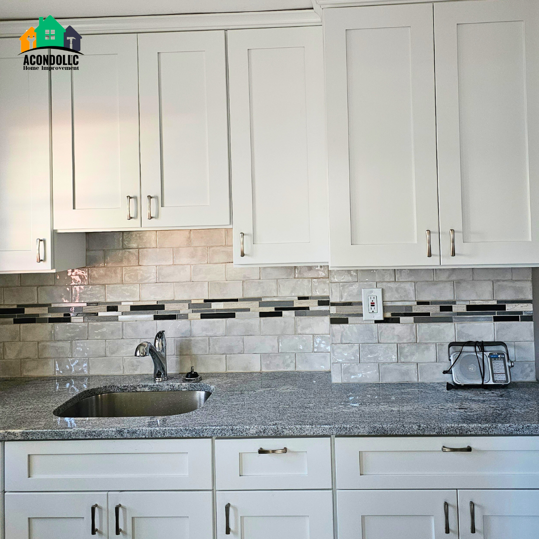 Kitchen countertop with white cabinets, a stainless steel sink, a faucet, beige tile backsplash with black and white accents, and a small radio on the right side.