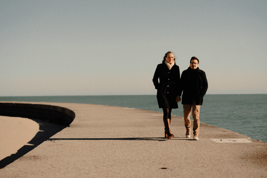 A man and woman walking hand in hand on a concrete pier by the ocean during the daytime.