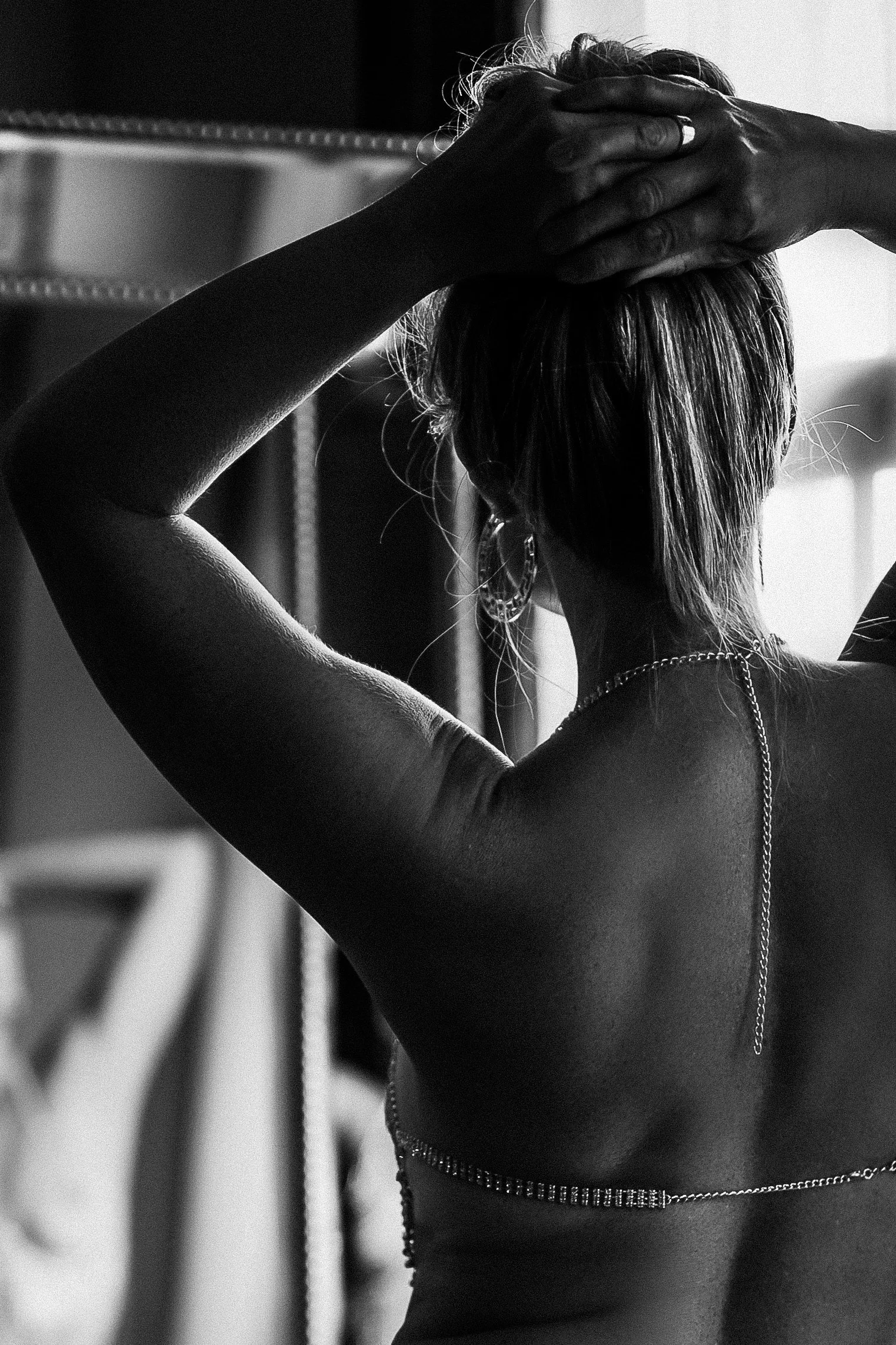 Luxury boudoir portrait of a woman leaning against the wall with a window behind her.