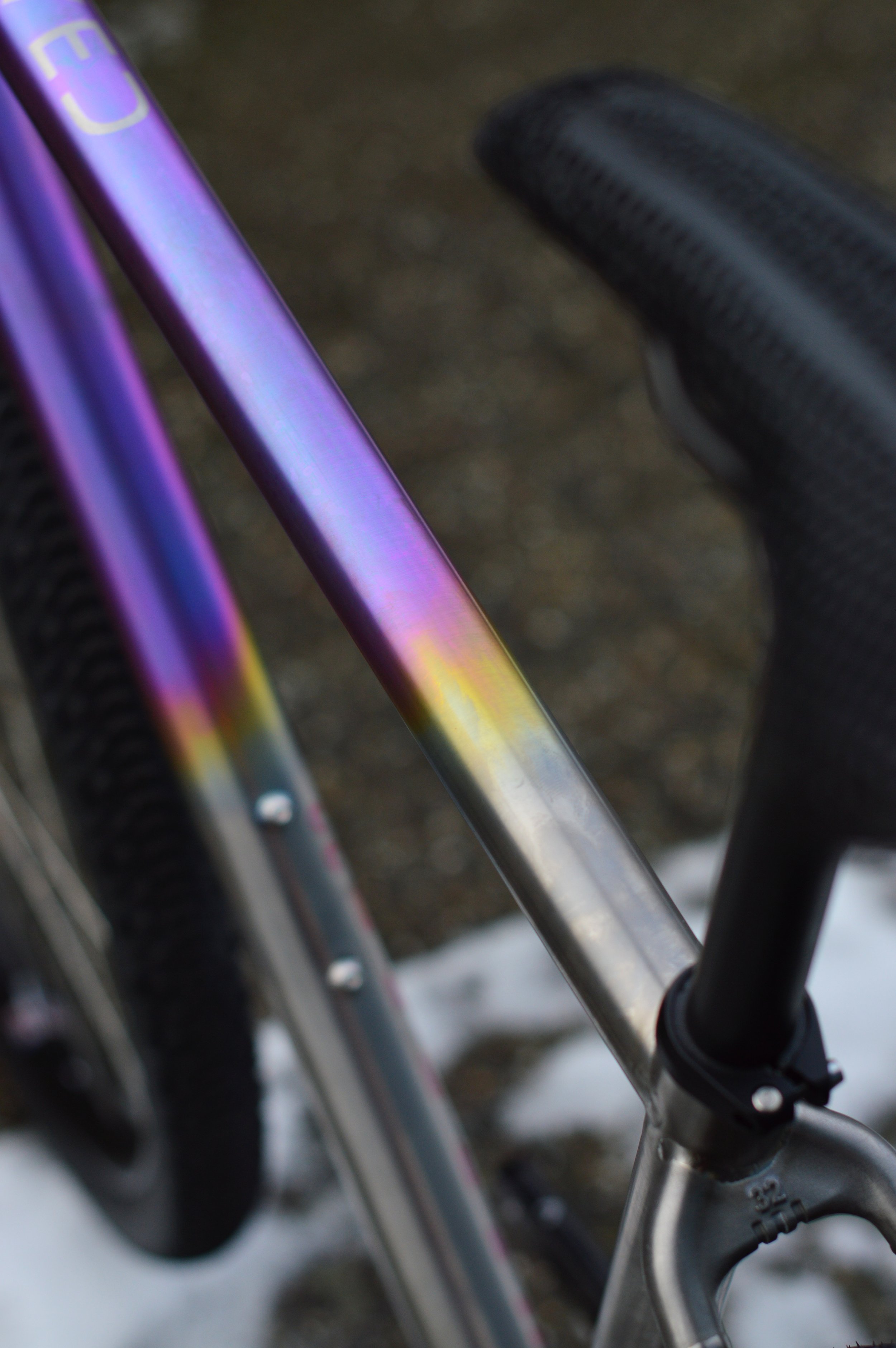 Close-up of a bicycle frame with iridescent purple and yellow coloring, focusing on the top tube and seat post.
