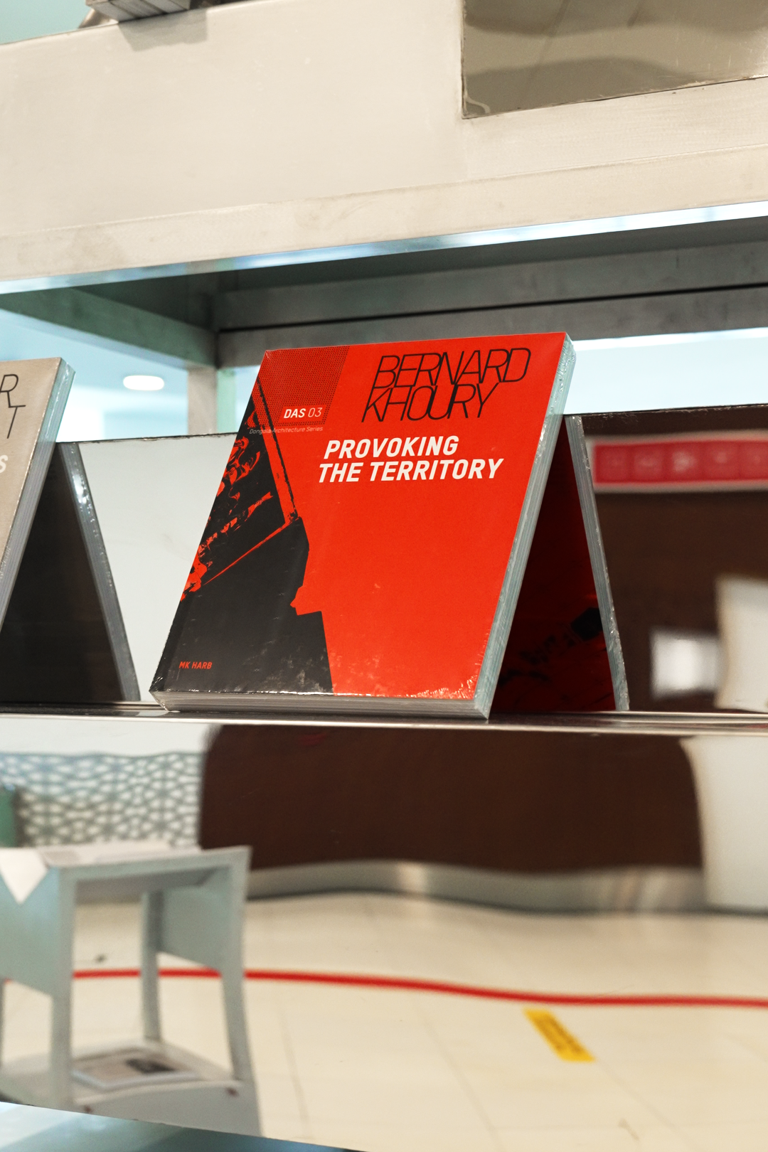 A red and black book titled 'Provoking the Territory' by Bernard Khoury displayed on a metal bookshelf.