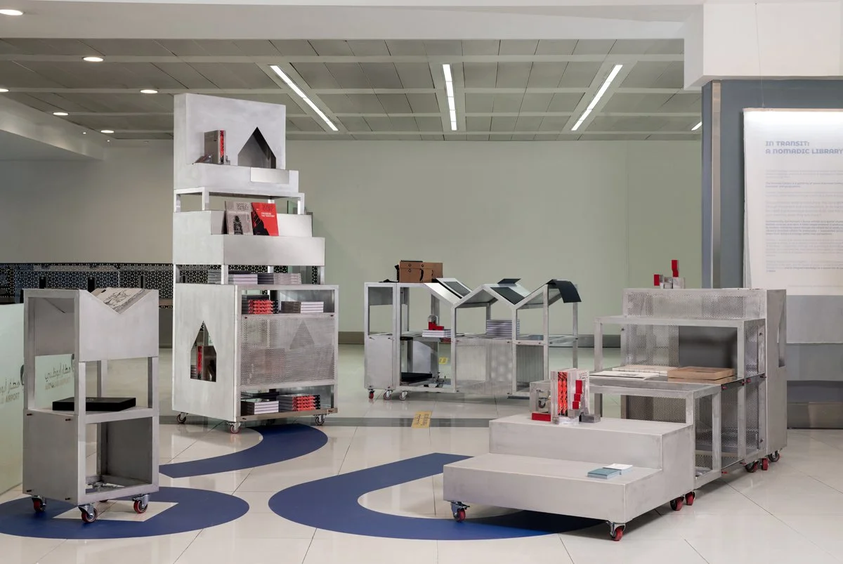 Etienne Bastormagi - Installation - A Nomadic Library -Empty modern library display area with metal shelving units on casters holding books and magazines, minimalistic design, clean white walls, and ceiling with integrated lighting.