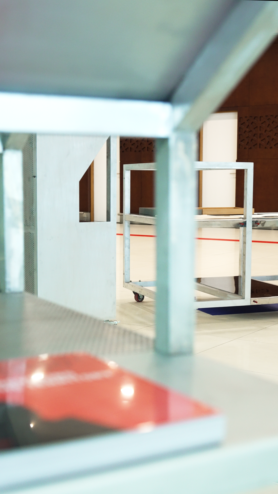 Close-up view of an indoor space with metal furniture, including tables and carts, seen through a metal railing or frame.