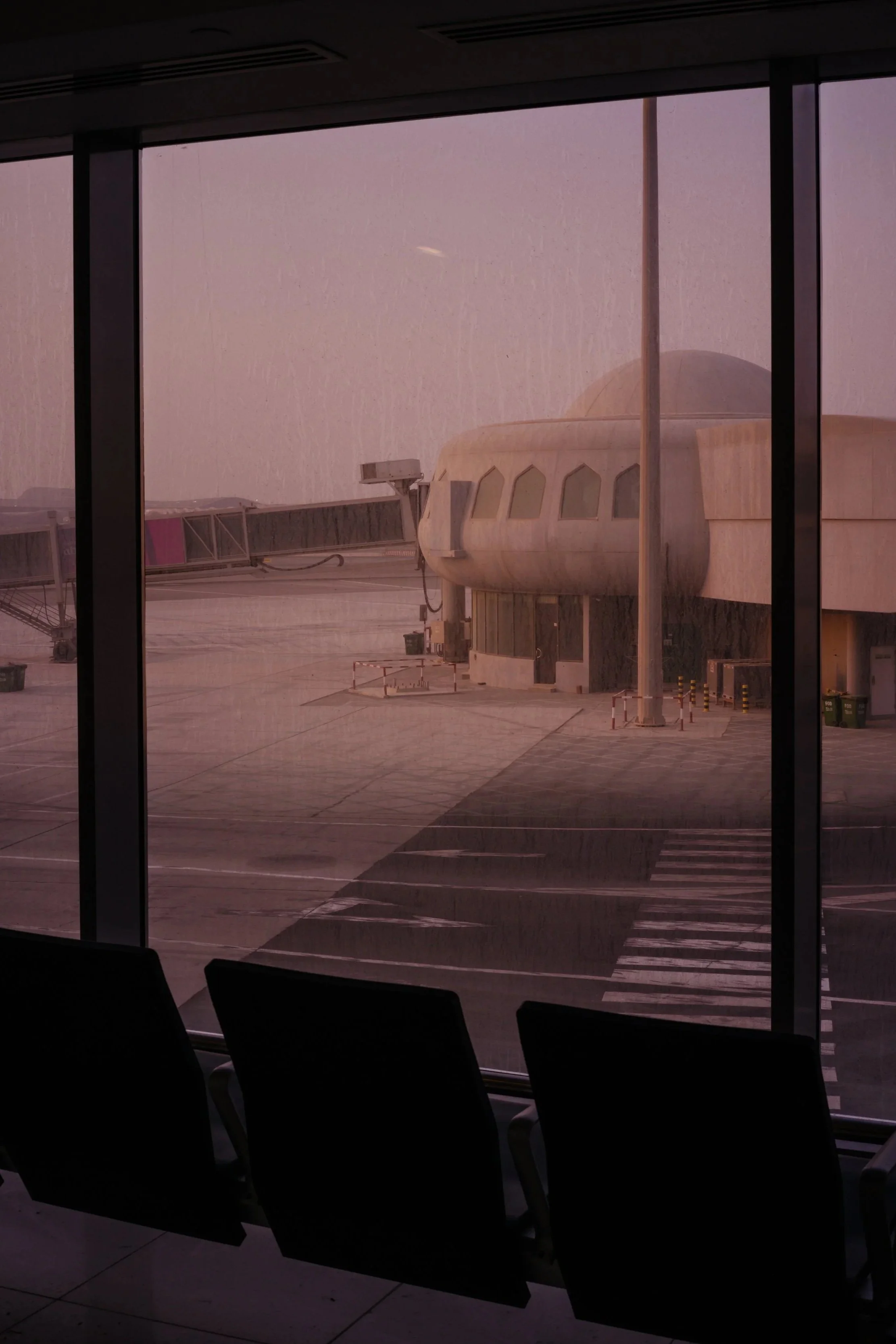 View of an airport terminal window showing an airplane on the tarmac during a rainy day, with rain streaks visible on the glass.