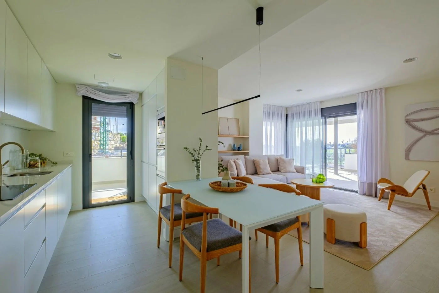 Bright, modern living room connected to a kitchen and balcony with glass doors and white curtains.