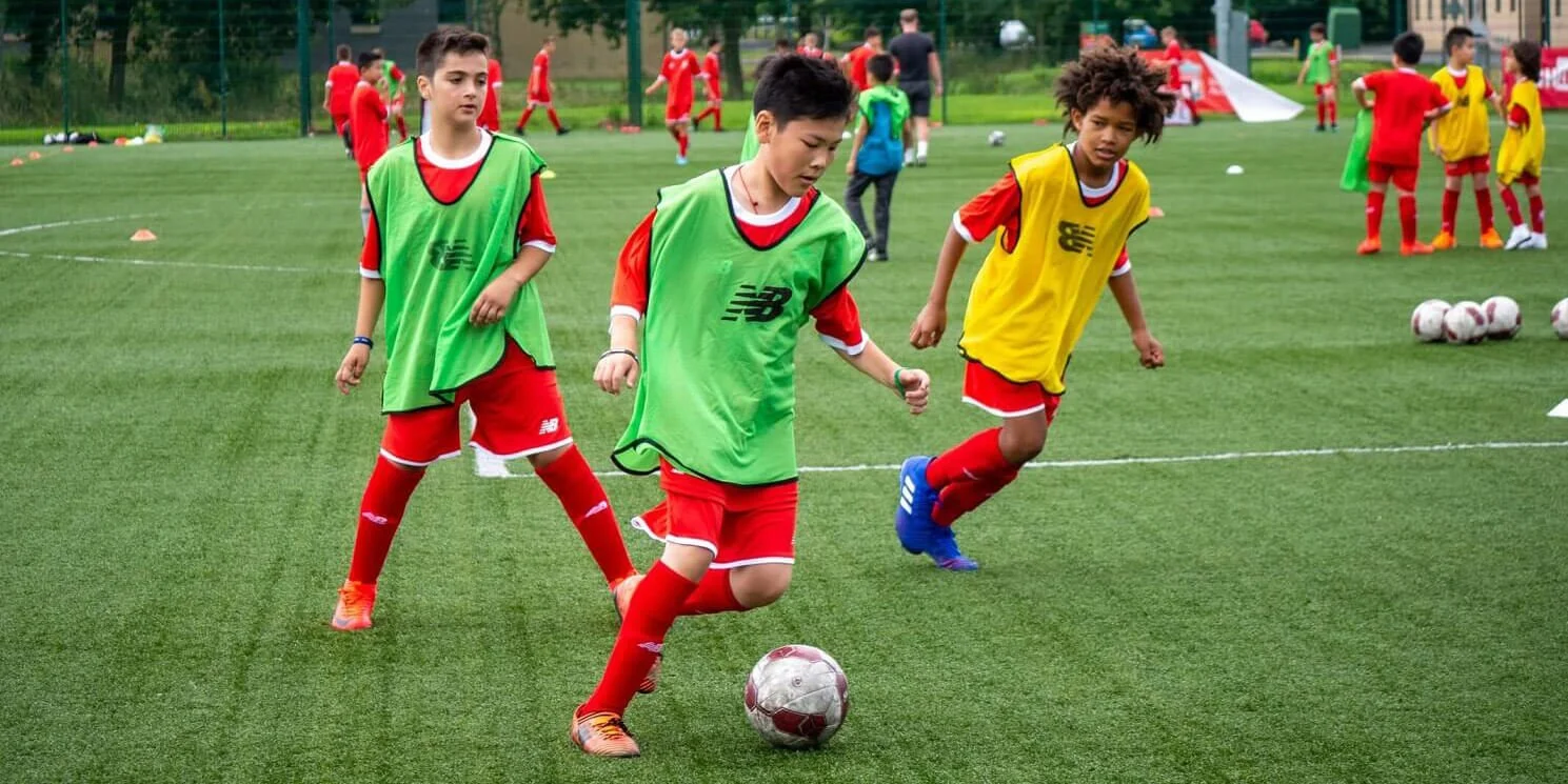 Children practicing soccer drills on a field during practice, with some dribbling the ball and others standing nearby.