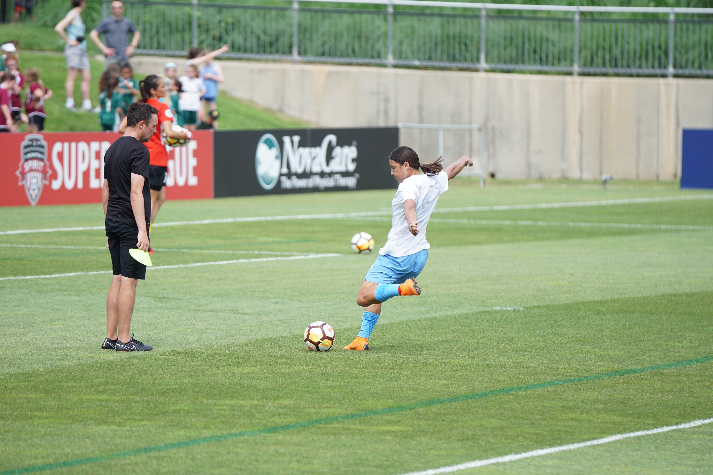 A soccer player kicks a ball during a game, while a referee and another player watch on the field.